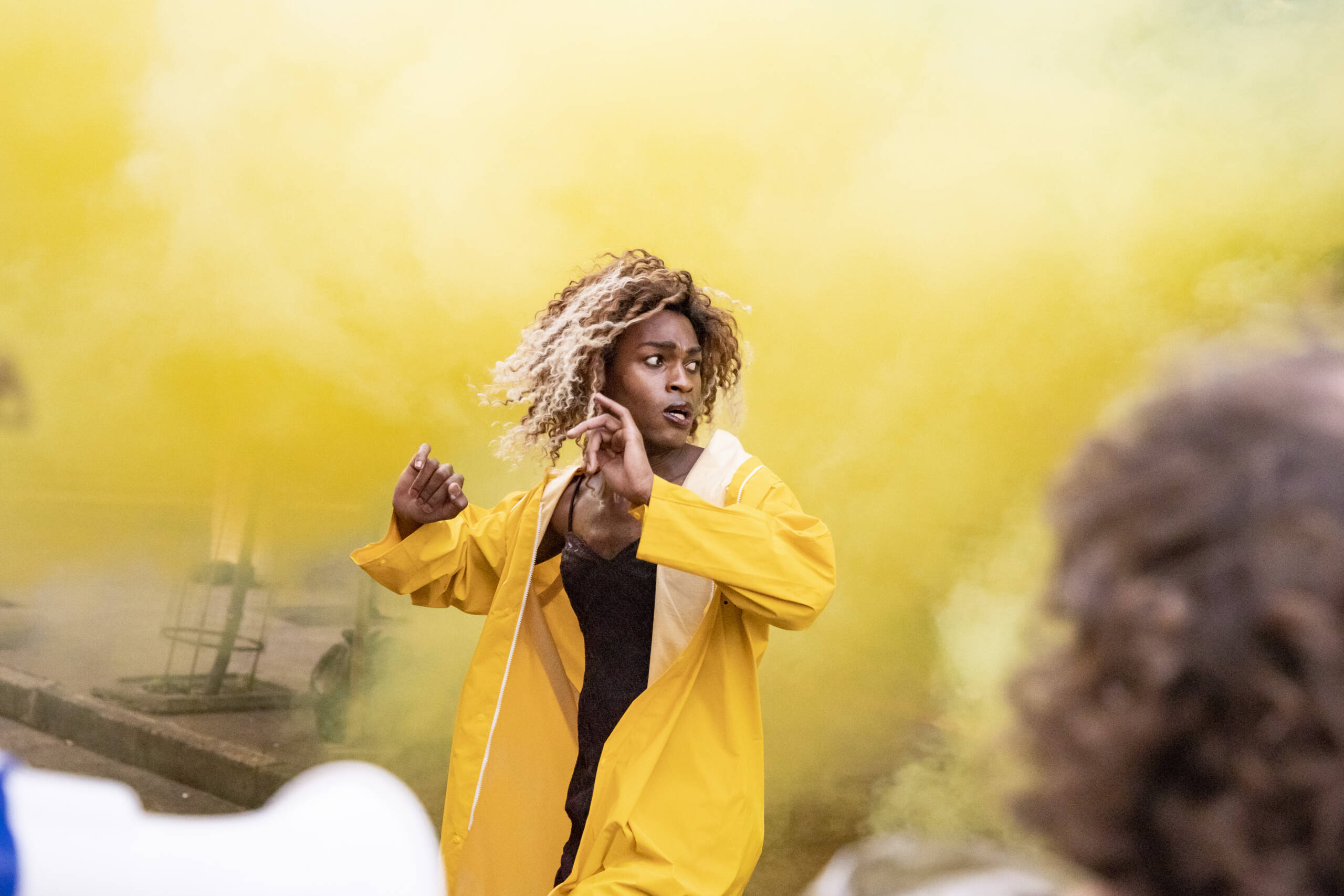 A performer in a bright yellow rain coat, standing in front of a big cloud of yellow smoke.